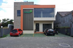 A modern building with a green logo, two parking spaces, and a brick facade.