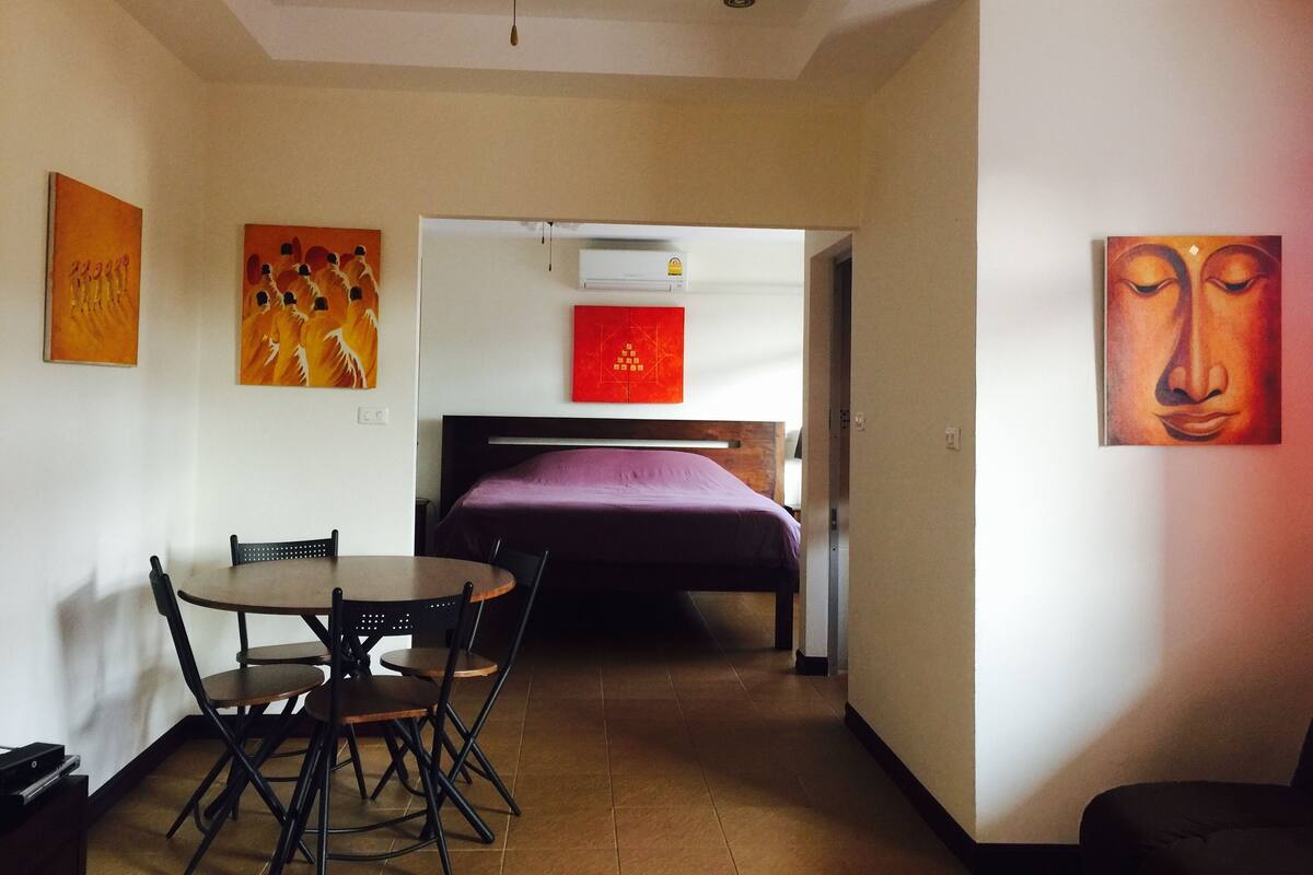 Una habitación con cama, una mesa de comedor con sillas y obras de arte en las paredes.