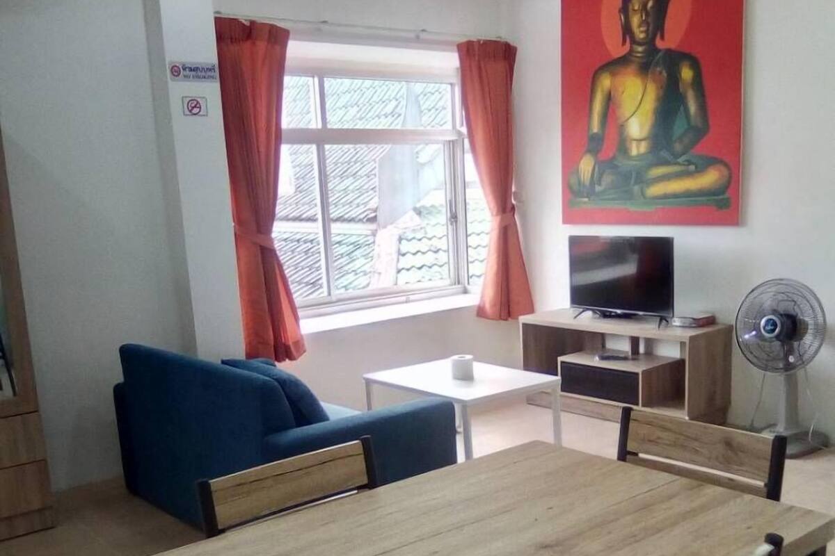 Sala de estar con una mesa de comedor de madera, sofá azul, televisor y una pintura de Buda.