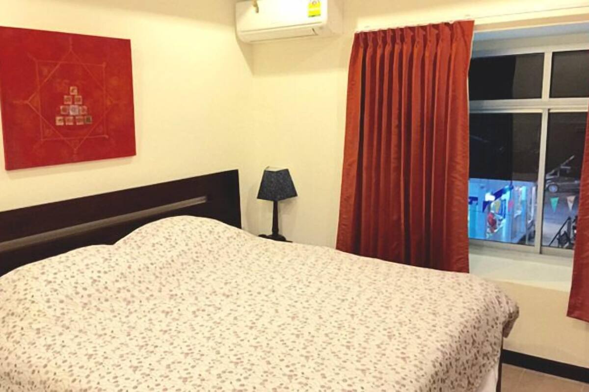 Habitación de hotel con cama, lámpara, ventana con cortinas y aire acondicionado instalado en la pared.