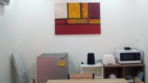 Una habitación pequeña y bien iluminada con una mesa y sillas de madera, un refrigerador, un microondas y una cafetera.