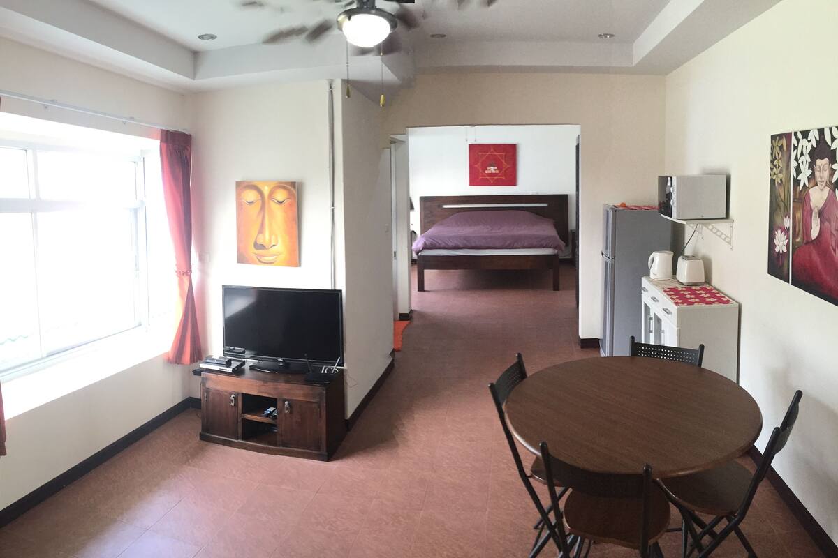 Una habitación con cama, televisor, mesa de comedor y refrigerador.