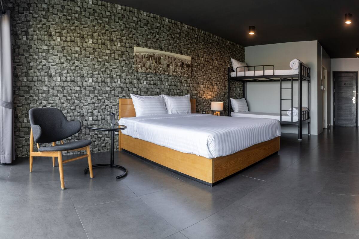 Een moderne hotelkamer met een stenen muur, een groot bed, een stoel, een klein tafeltje en een stapelbed.