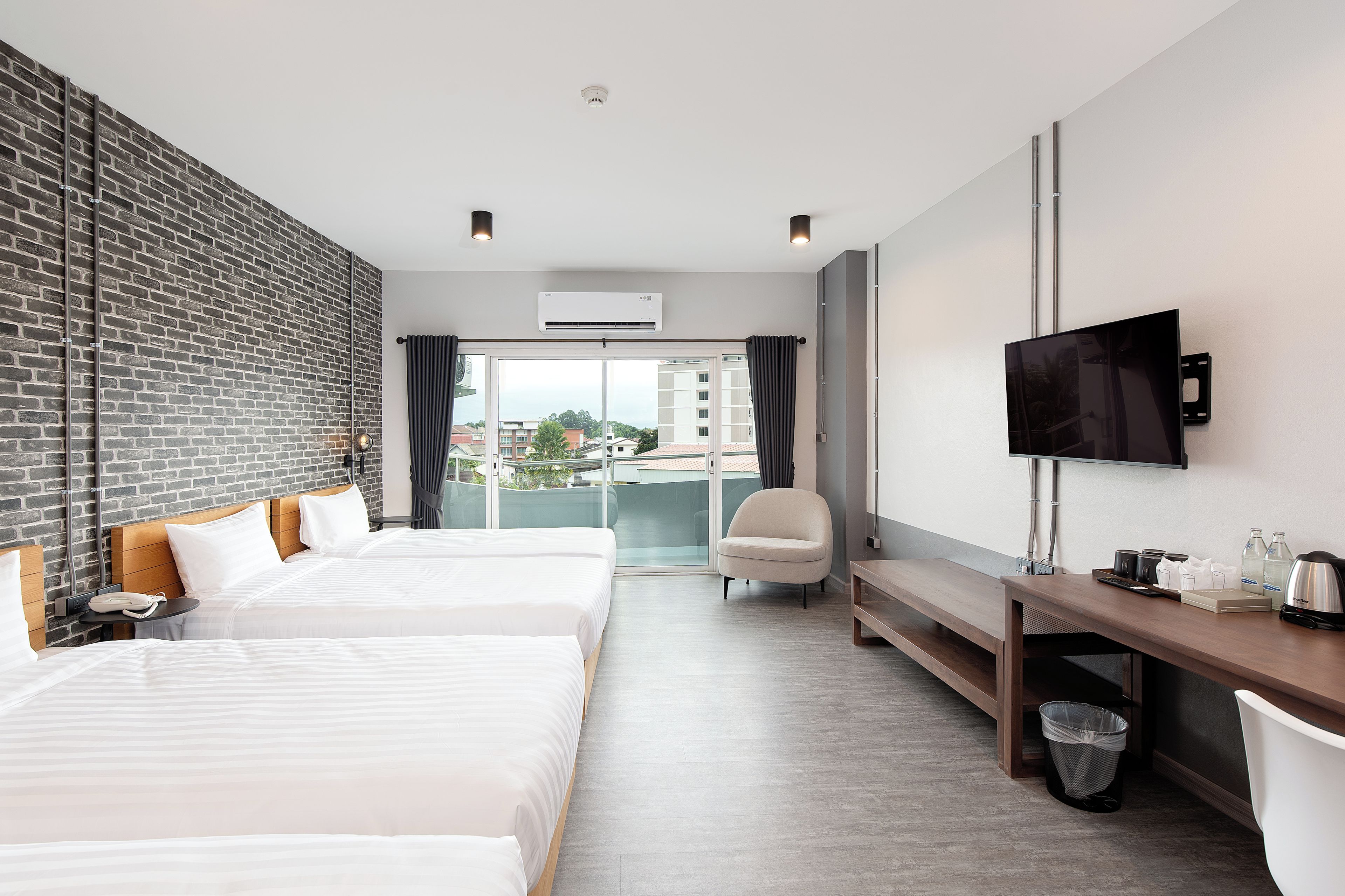 A hotel room with two beds, a desk, a chair, a TV, and a view of the city.