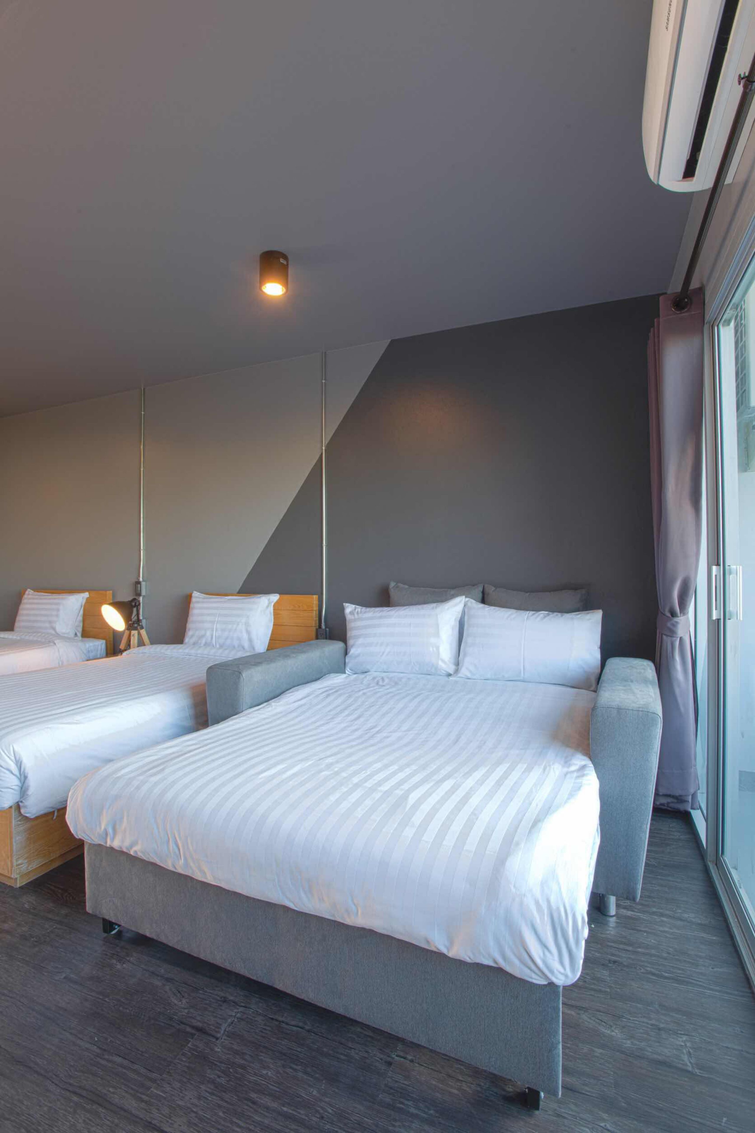A hotel room with two beds, a sofa, a large window, and an air conditioning unit.