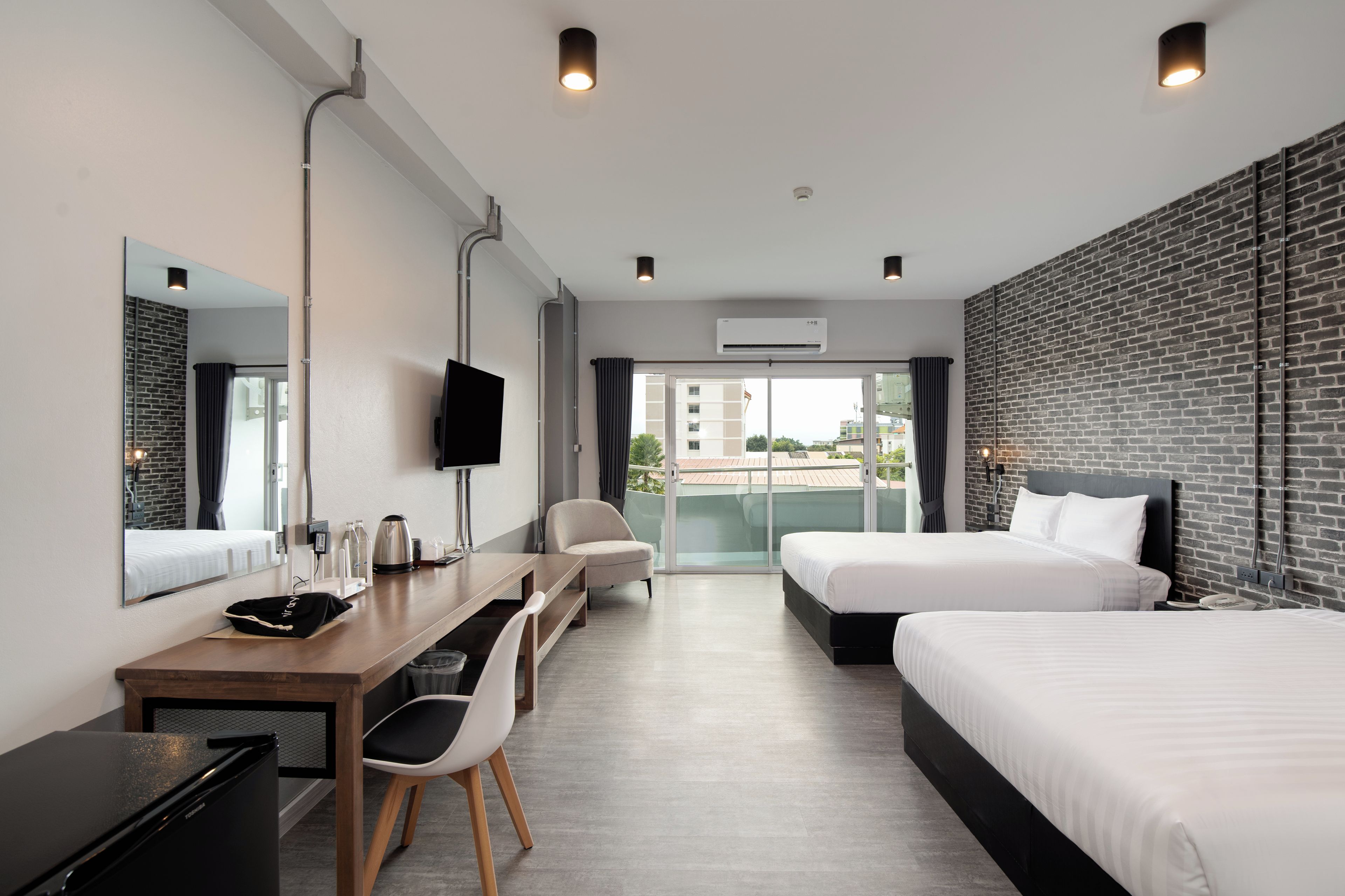 Et moderne hotelværelse med skrivebord, to senge, fjernsyn og en balkon med udsigt.