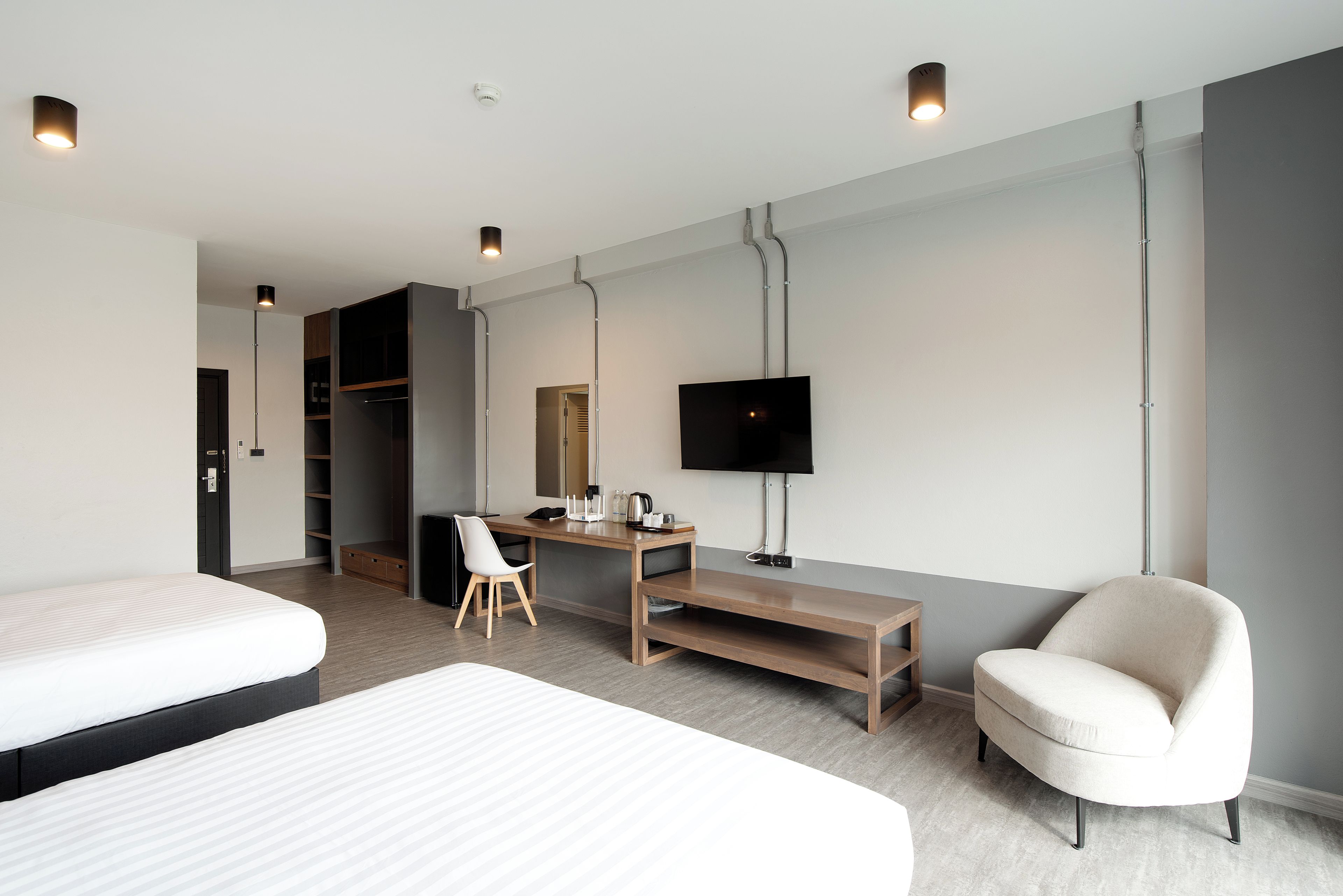 A modern hotel room with a bed, a desk, a chair, a TV, and a wardrobe.