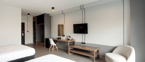 A modern hotel room with a bed, a desk, a chair, a TV, and a wardrobe.