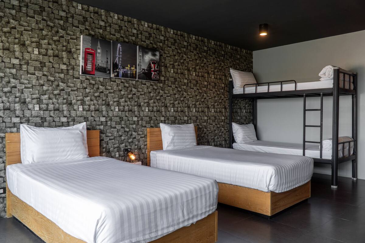 Een kamer met twee eenpersoonsbedden, een stapelbed en een stenen muur met foto’s.