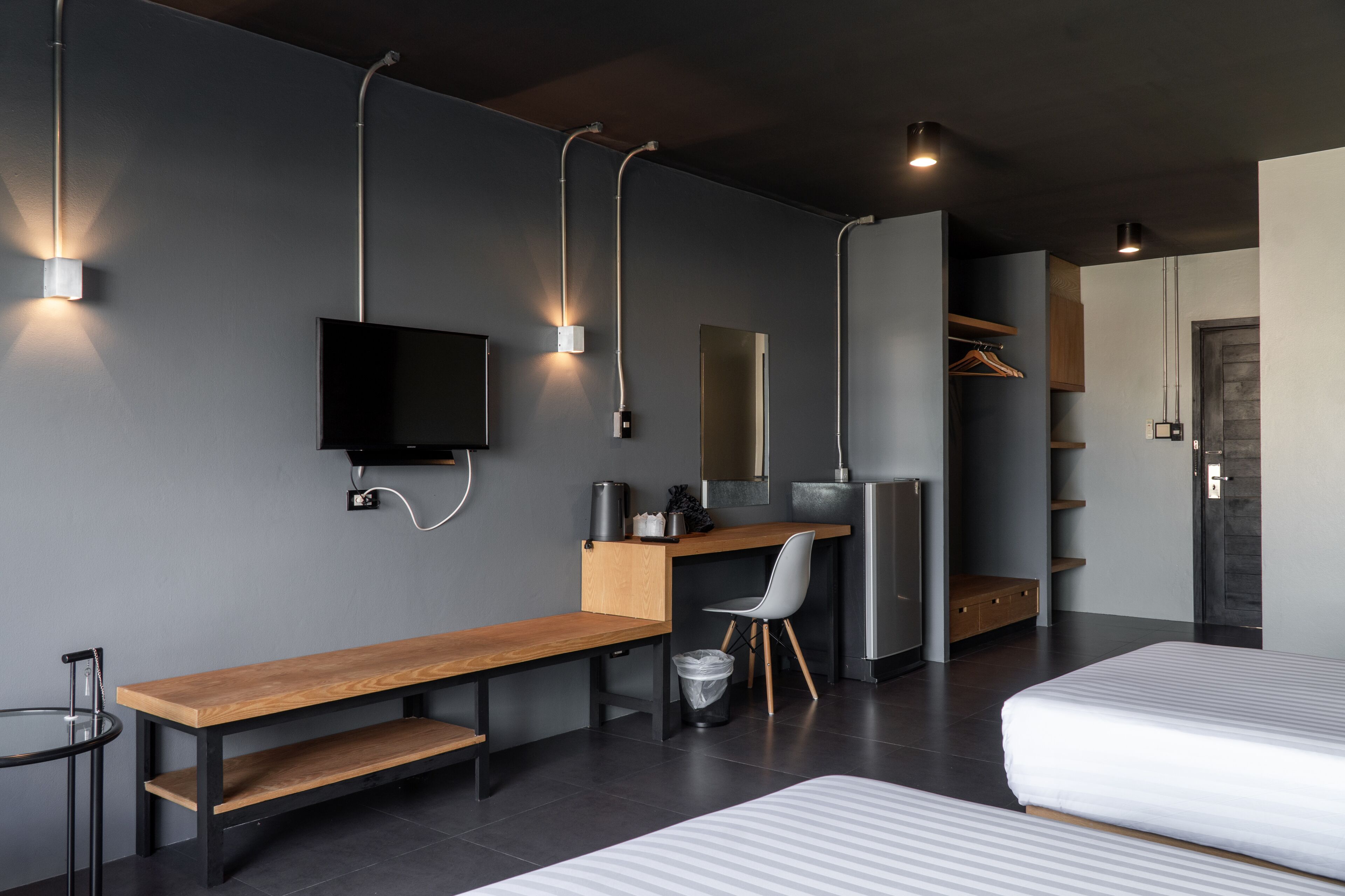 A modern hotel room with a wooden desk, a television, a bed, and built-in shelving.