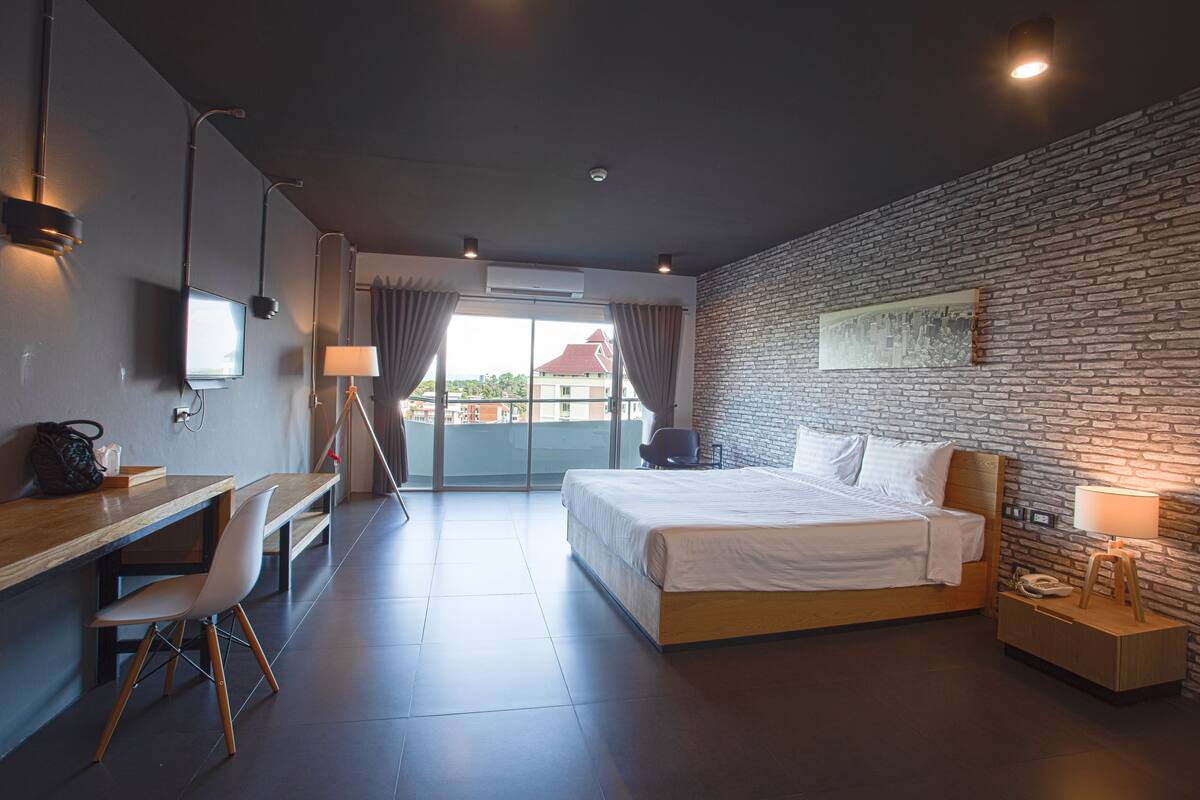 Een moderne hotelkamer met een groot bed, een bureau en een stoel. Er is uitzicht op de stad vanuit het raam.