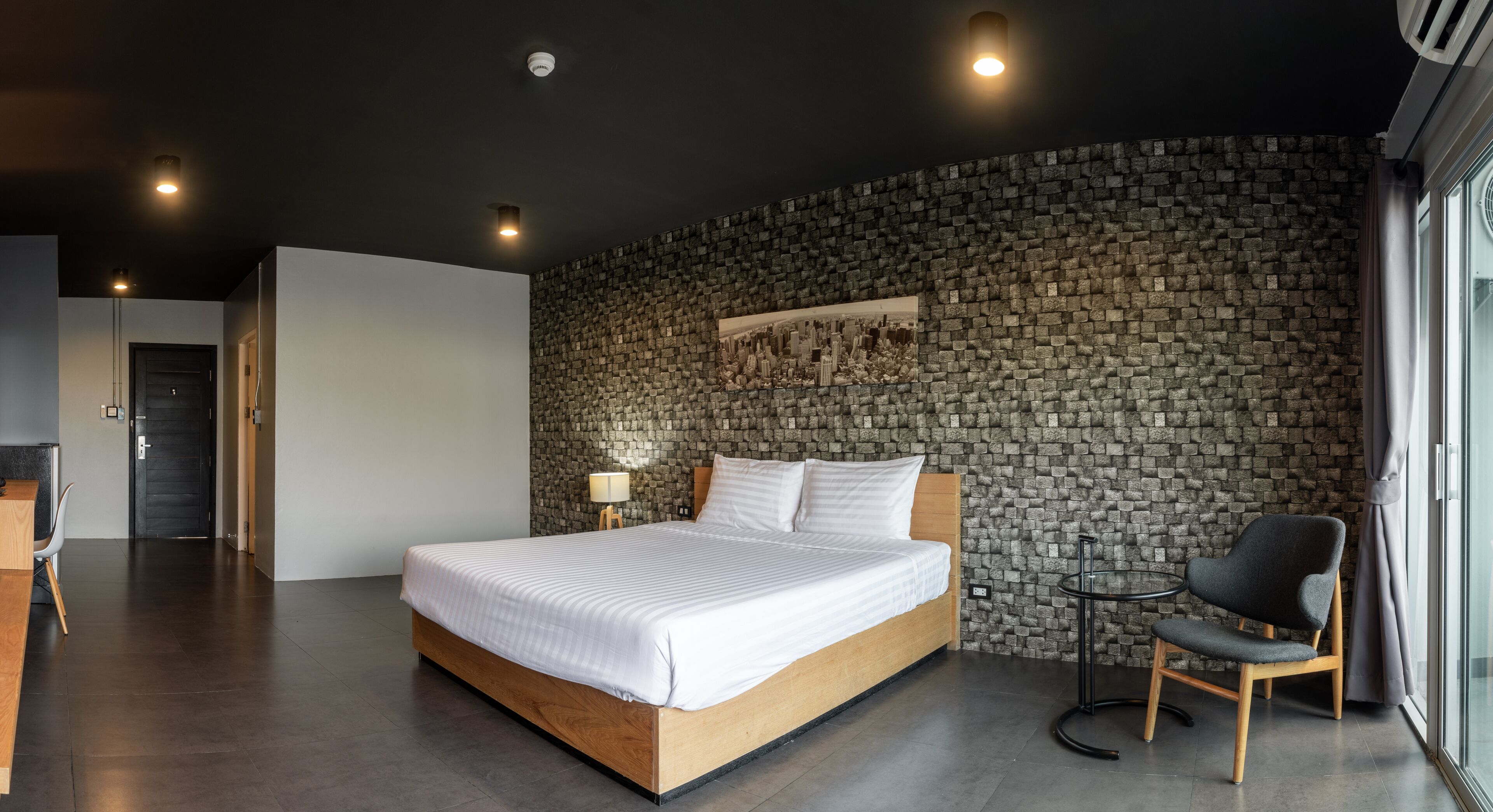 A modern bedroom with a stone wall, a wooden bed, a small round table, and a chair.