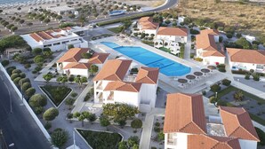 An aerial view of a resort with a swimming pool, white buildings with red-tiled roofs, and a beach area. - Fito Aqua Bleu Resort (Samos)