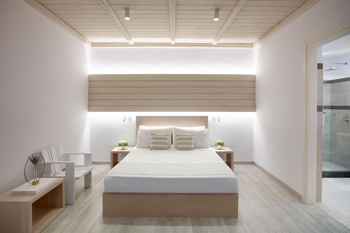 Un dormitorio moderno con una cama grande, mesitas de noche, un banco y una zona de ducha de vidrio.