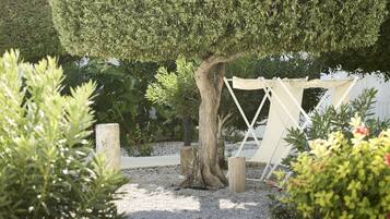 Un jardín cuidado con un seto ordenado, un tronco de árbol de madera y un columpio blanco.