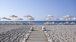 A beach with a wooden pathway leading to the sea, lined with beach chairs and umbrellas. - Fito Aqua Bleu Resort (Samos)