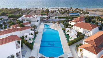 A resort with a swimming pool, beach, and white buildings with red roofs.