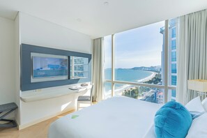 A hotel room with a large bed, a desk with a computer, and a TV displaying a cityscape. - Diamond Bay Hotel (Nha Trang)