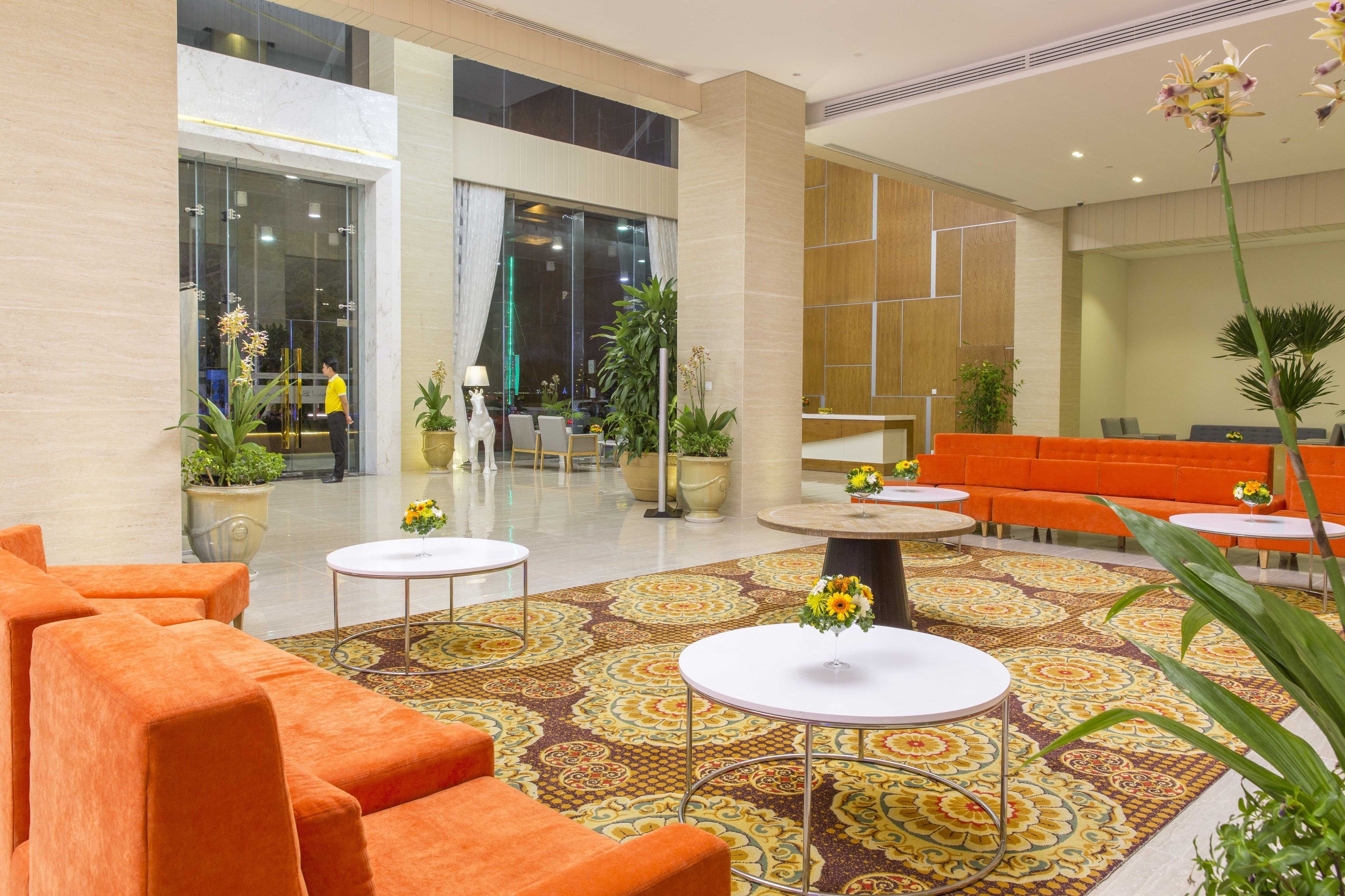 A lobby with orange seating, a patterned carpet, and potted plants.