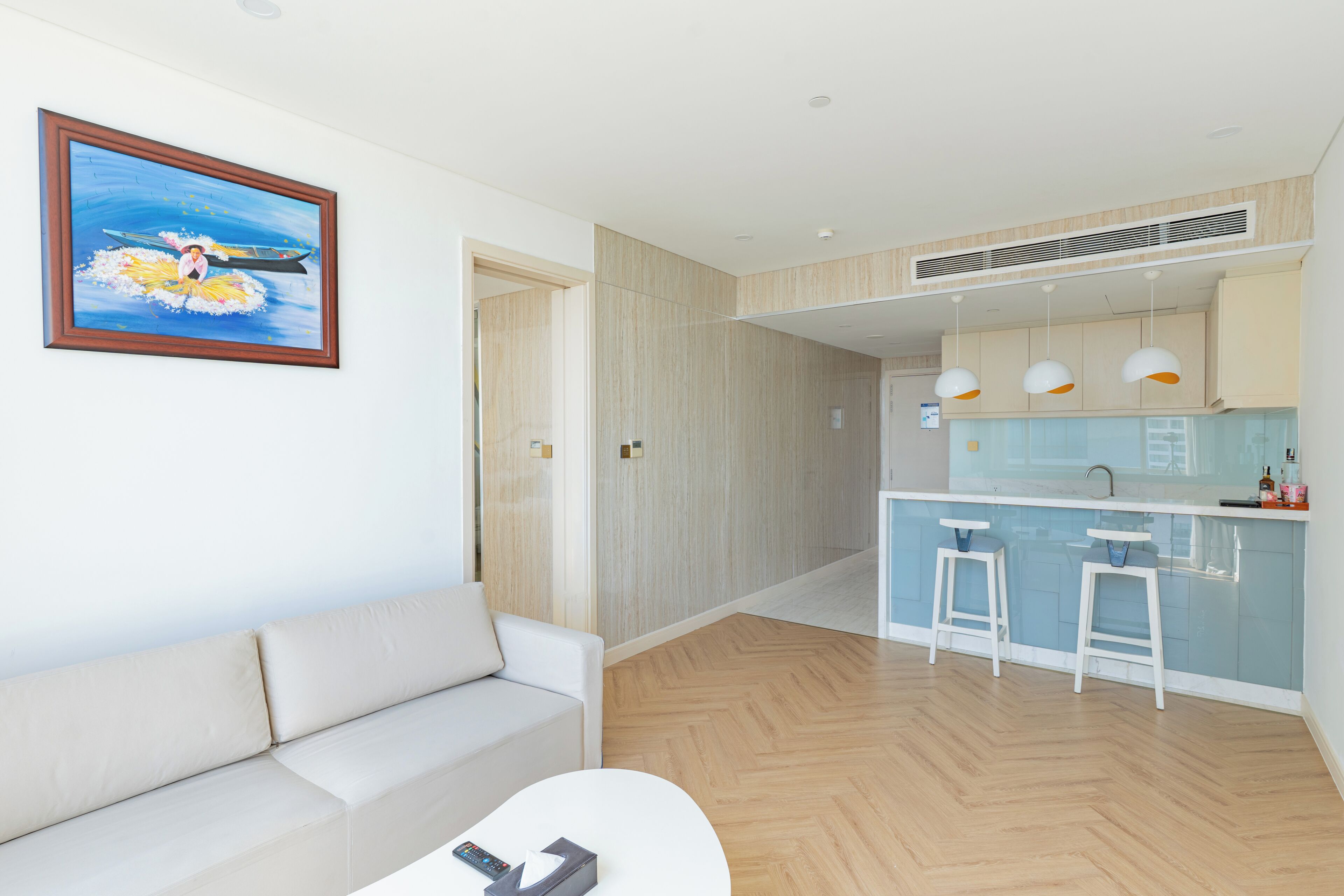 A modern living room with a sofa, a coffee table, and a kitchen with bar stools.