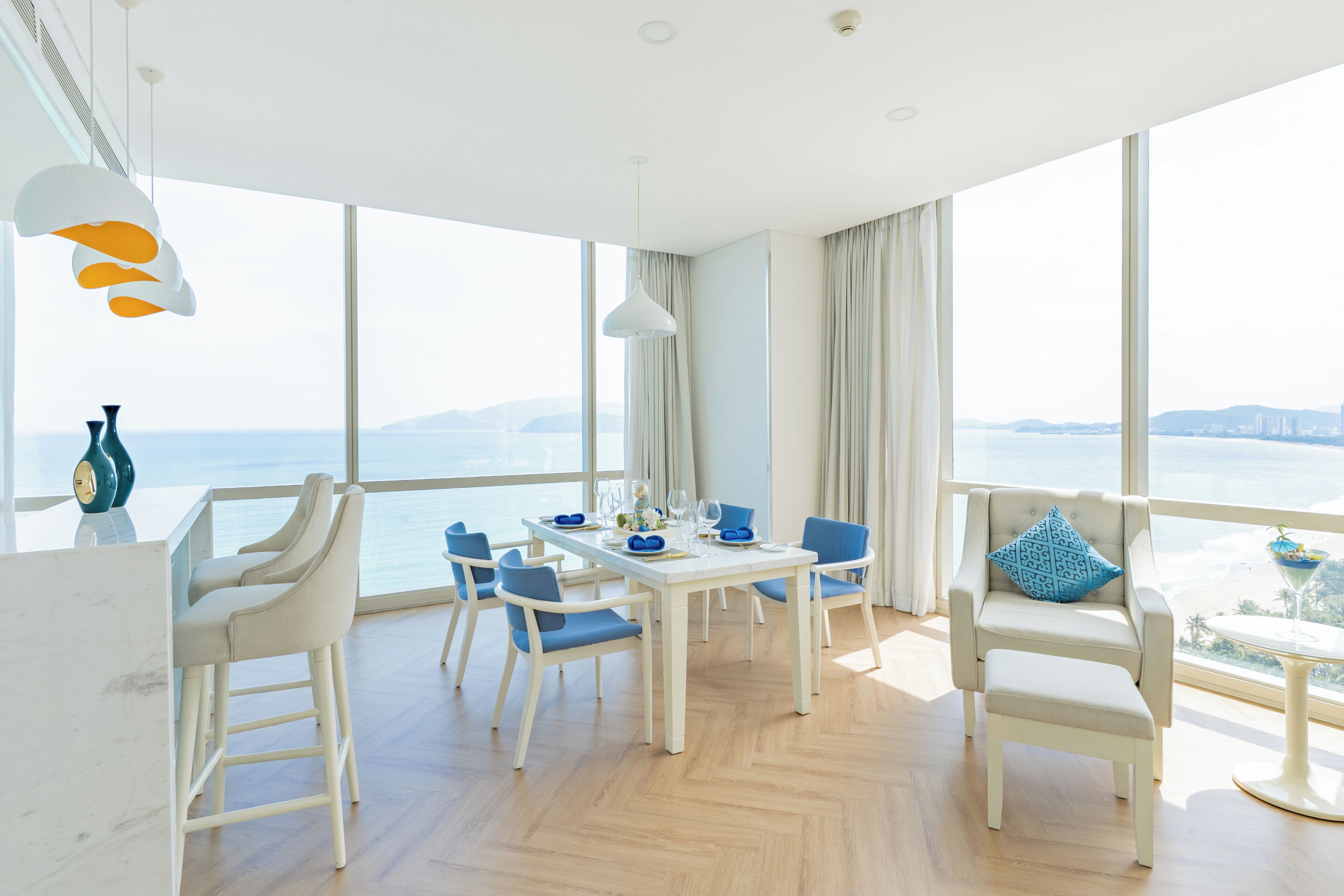 A modern dining area with a view of the sea, a white table set with blue chairs, and a balcony with a view.
