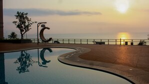 A pool with a curved edge, a metal sculpture, and a sunset view. - Diamond Bay Hotel (Nha Trang)