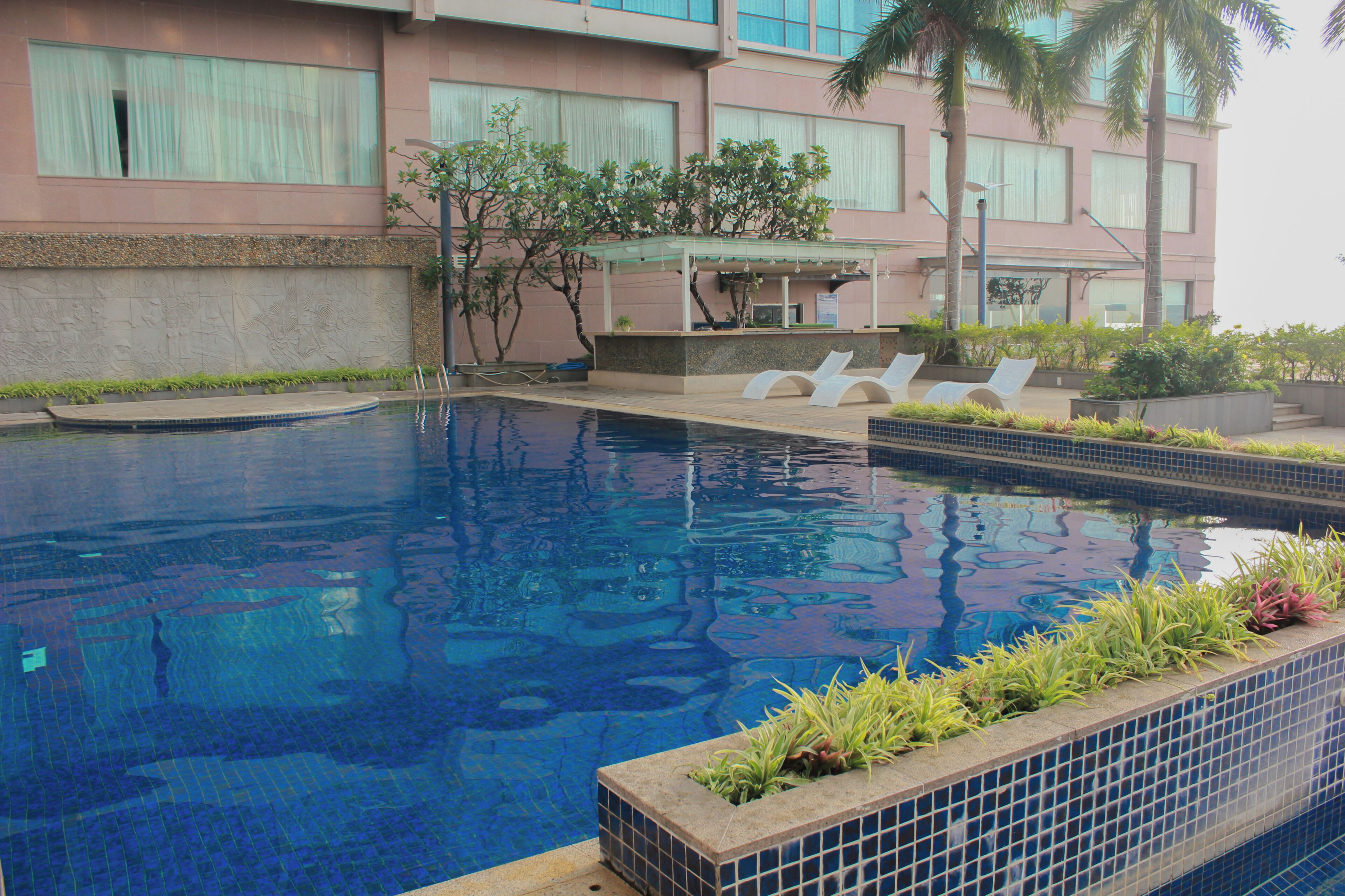 A swimming pool with lounge chairs, a covered seating area, and a building with large windows and a stone facade.