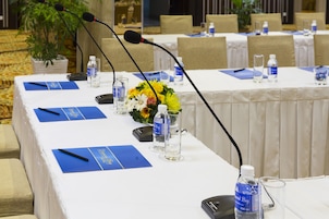 Une table de conférence équipée de microphones, de bouteilles d’eau et de porte-noms bleus.