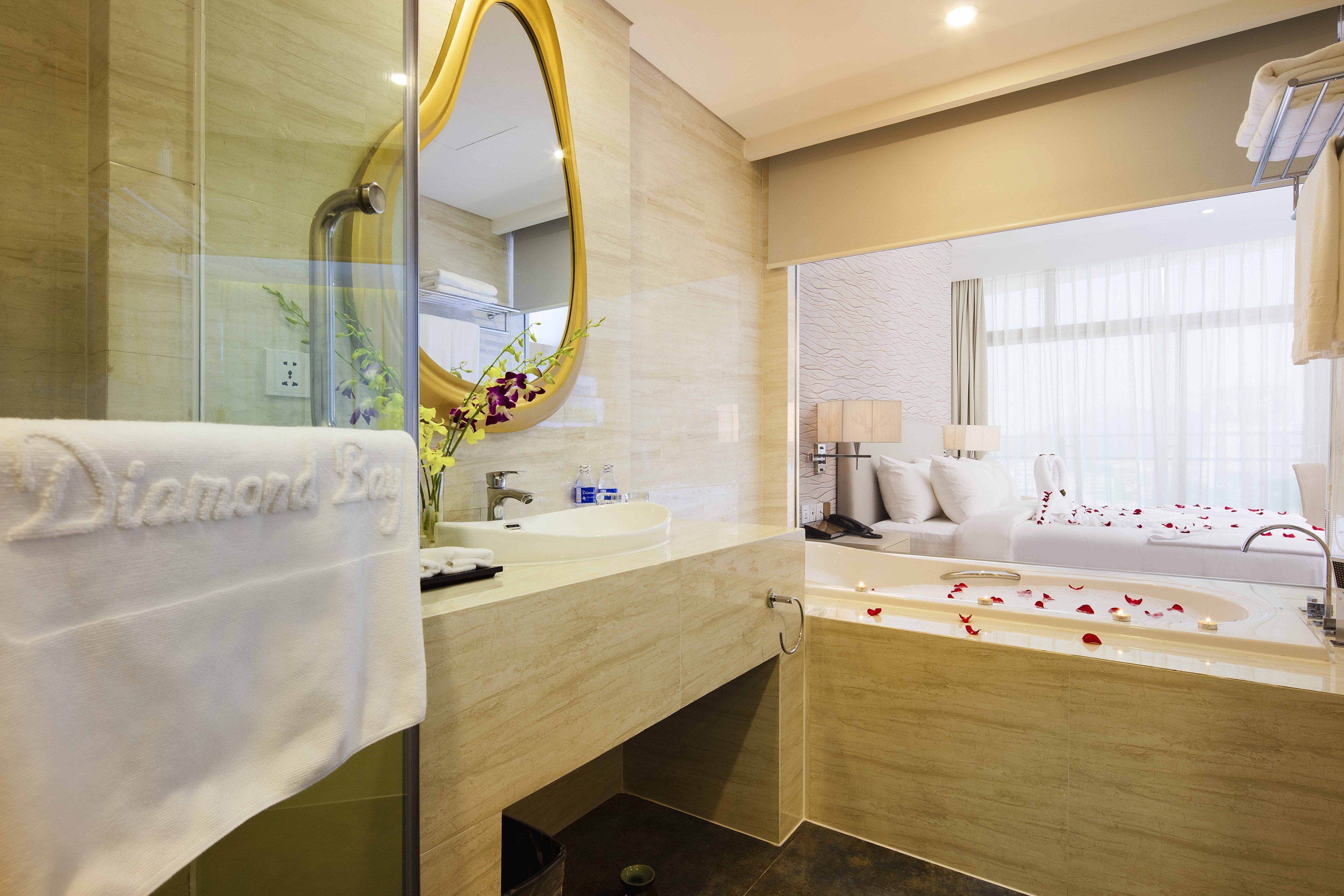 Une salle de bain moderne avec un grand miroir ovale, une baignoire remplie de pétales de roses, un lavabo et un espace douche.