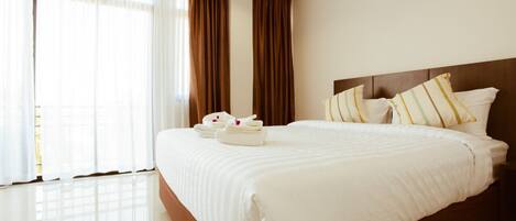 A hotel room with a large bed, curtains, and a neatly made bed with towels.