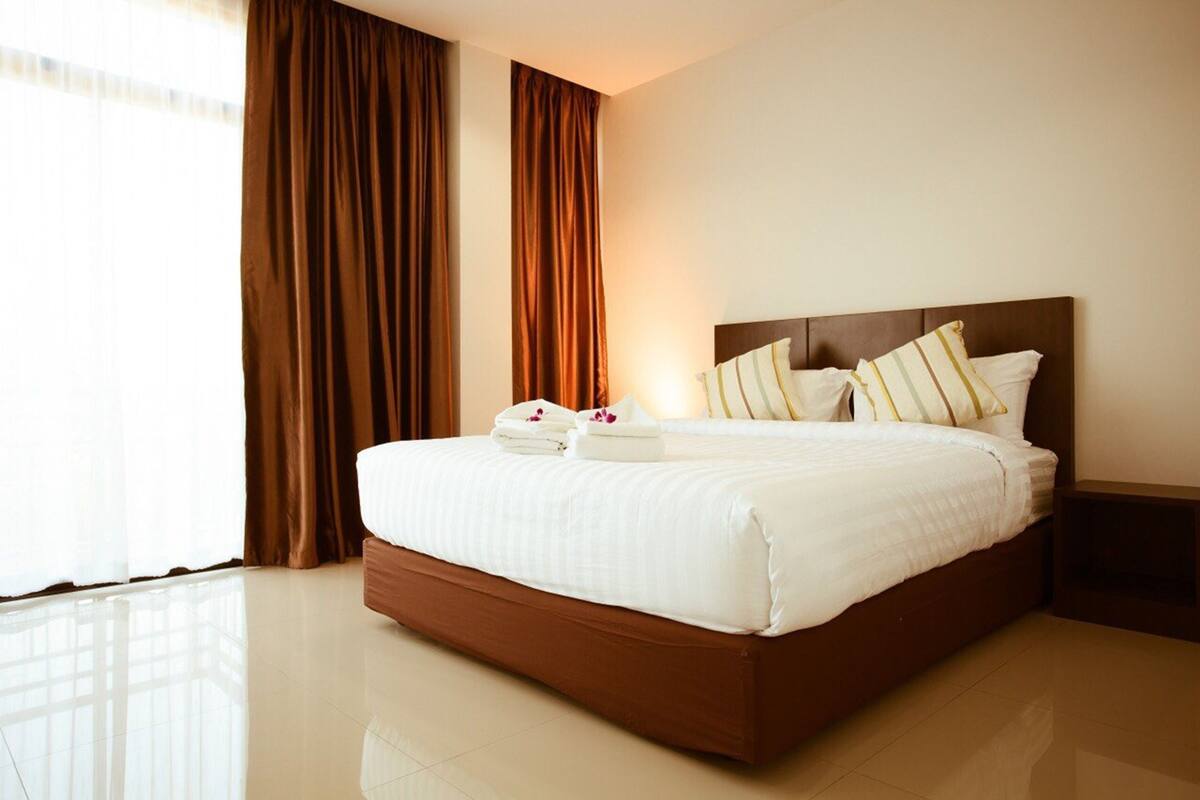 A hotel room with a large bed, brown curtains, and a nightstand.