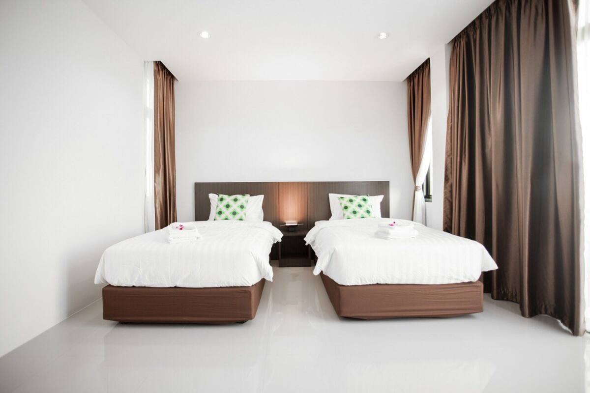 A hotel room with two beds, a large window, and brown curtains.