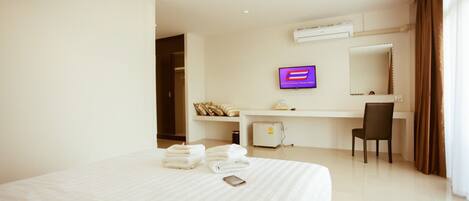 A hotel room with a large bed, a desk with a computer, a chair, and a TV on the wall.