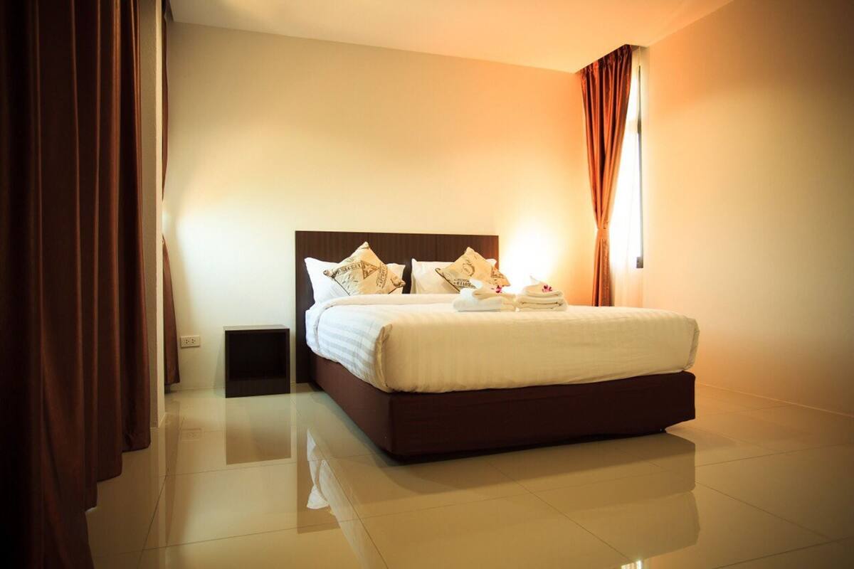 A hotel room with a large bed, a bedside table, and a window with curtains.