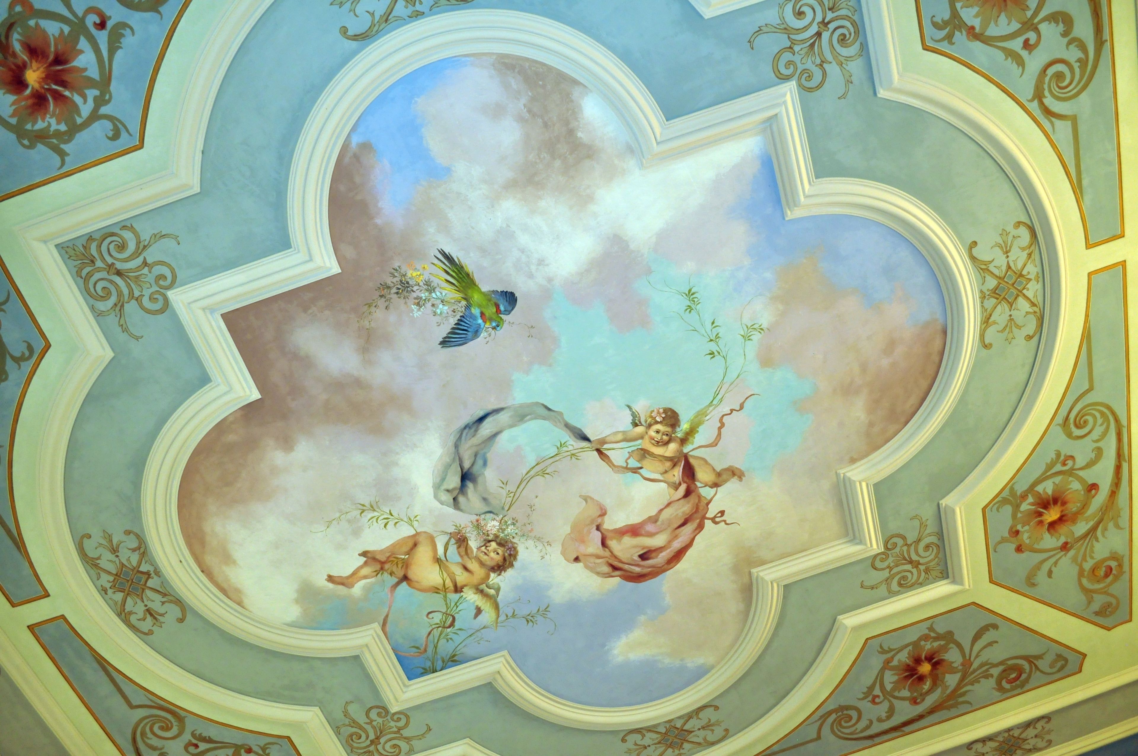 Un techo con un fresco decorativo que muestra querubines y un pájaro.