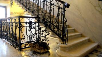 Una escalera de mármol con barandillas de metal negro ornamentado y una base de piedra decorativa.