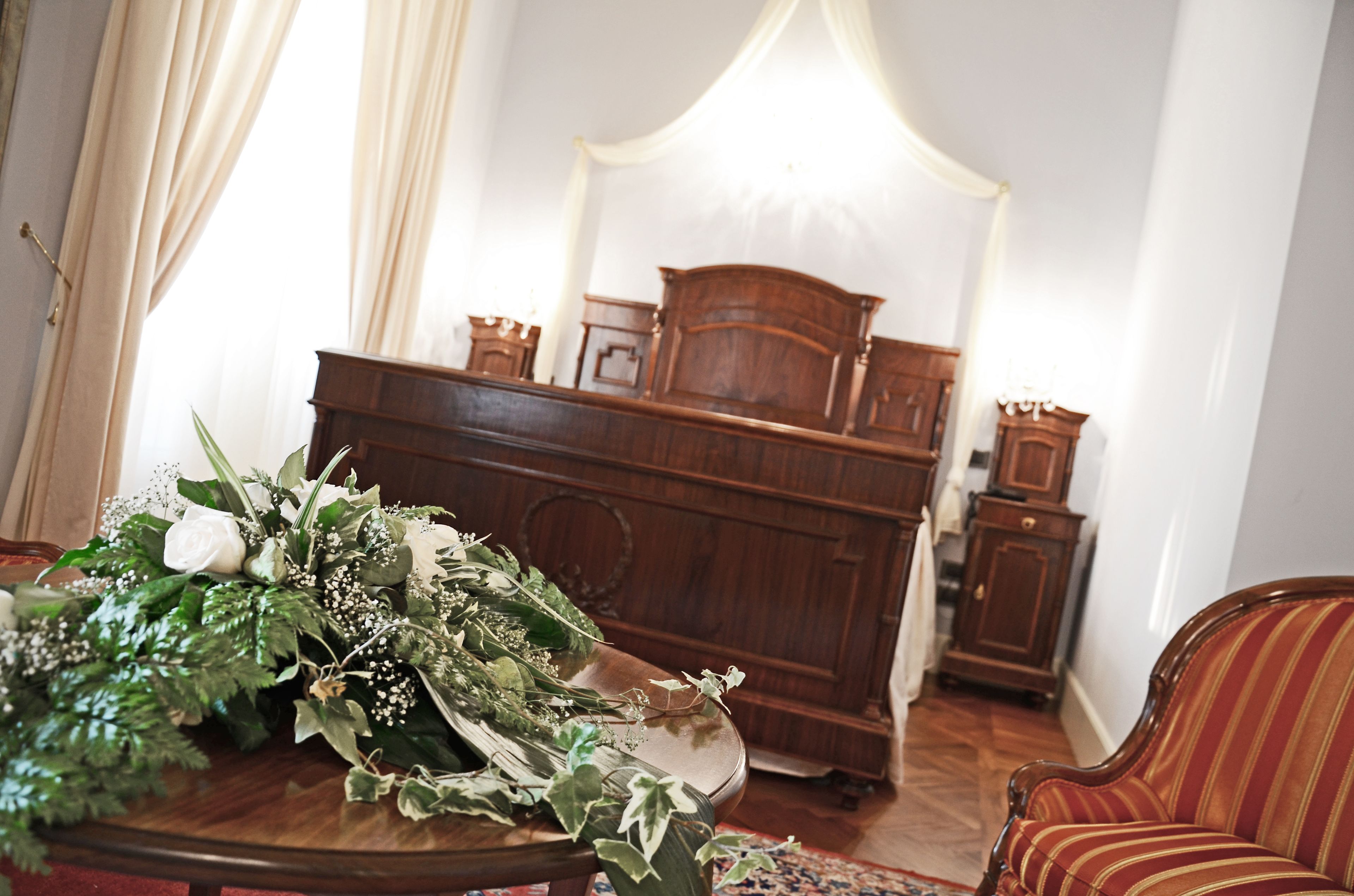 Ein Zimmer mit einem hölzernen Klavier, einer Blumenkomposition auf einem Tisch und einem gestreiften Sessel.