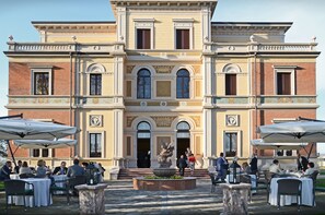 Un bâtiment historique doté d’une entrée principale, d’un espace extérieur aménagé pour s’asseoir et d’une fontaine.