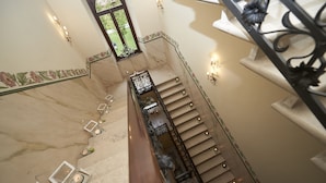 Un escalier en marbre avec une rampe, une petite table avec une bougie et des appliques murales.