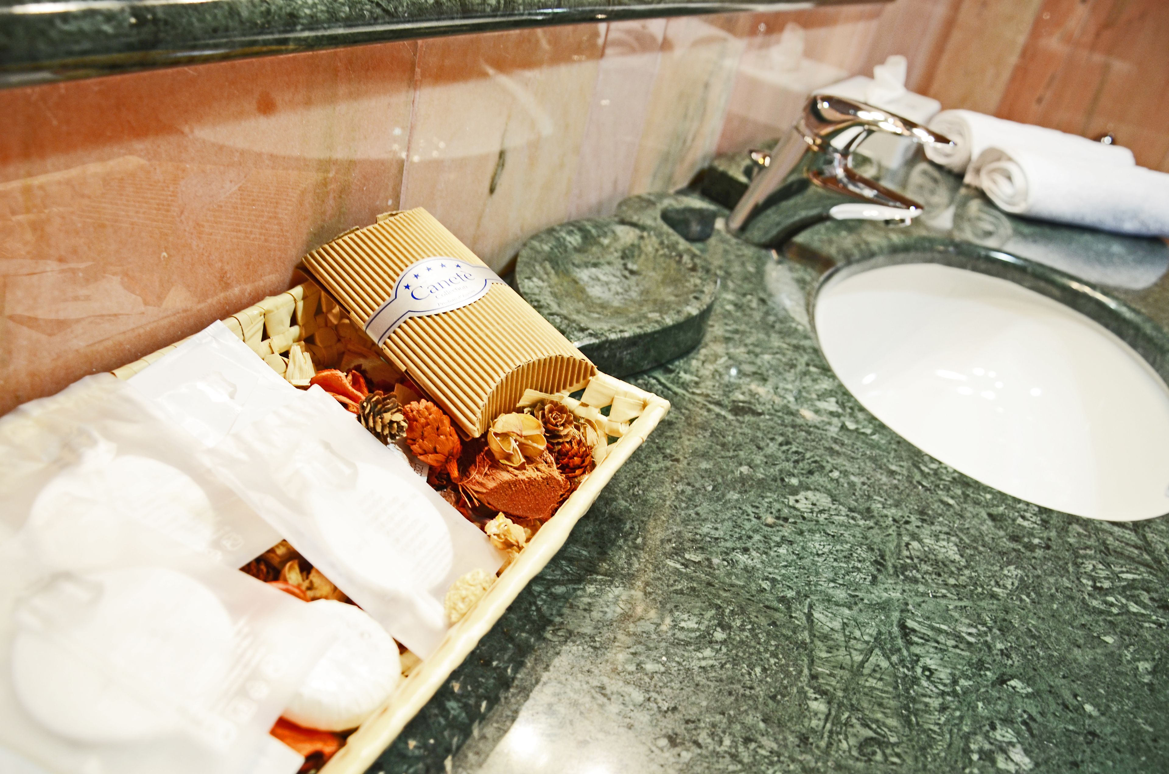 Casa de banho com bancada de granito, lavatório branco e bandeja de madeira com artigos de higiene pessoal.