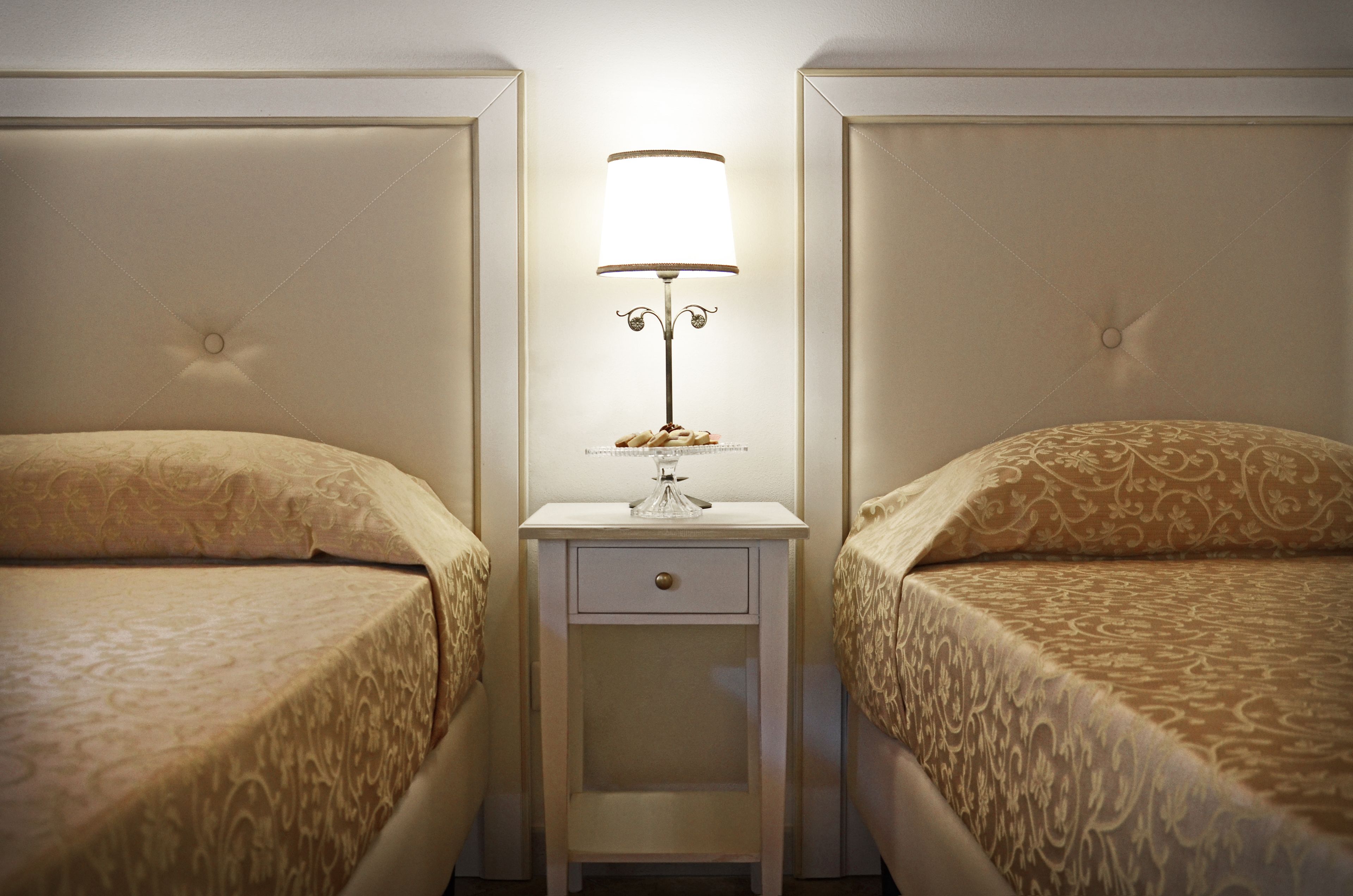 Quarto de hotel com duas camas, uma mesa de cabeceira com abajur e uma gaveta.