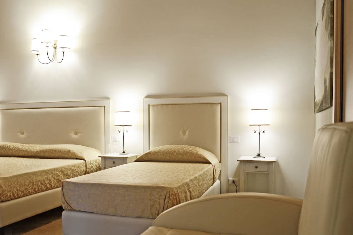 A hotel room with two beds, each with a headboard and bedside tables with lamps.