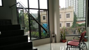 Un interior espacioso con una escalera que lleva a un balcón, ventanas amplias con vistas a edificios y áreas verdes.