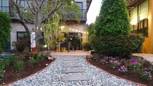 A well-maintained garden pathway leading to a building entrance, surrounded by lush greenery and flowering plants. - The Bike Loft Family Hostel (Hua Hin)