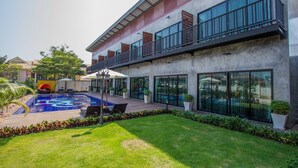 A modern building with a swimming pool, outdoor seating, and a well-maintained lawn. - The Bike Loft Family Hostel (Hua Hin)