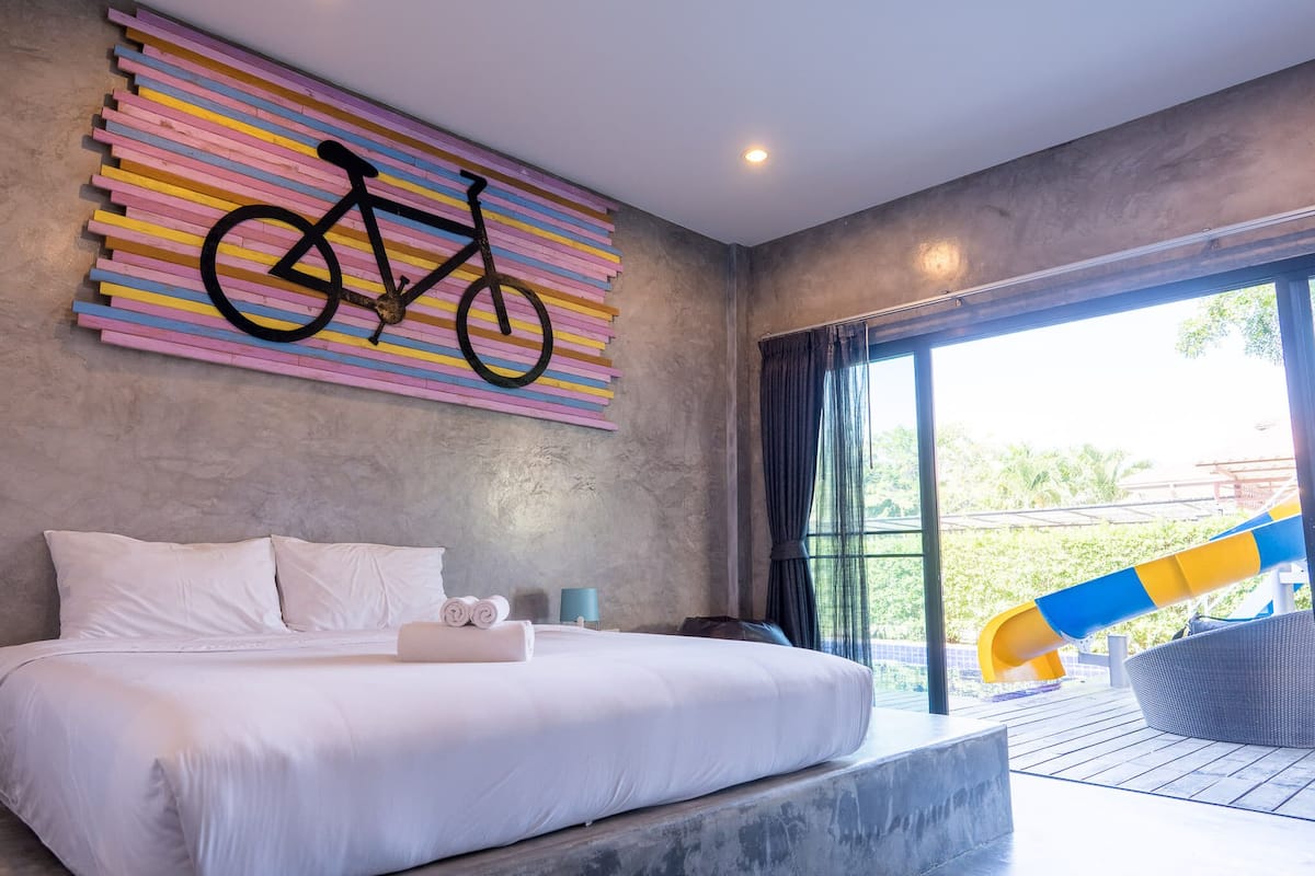 A modern hotel room with a large bed, a bicycle-themed artwork, and a view of a slide.
