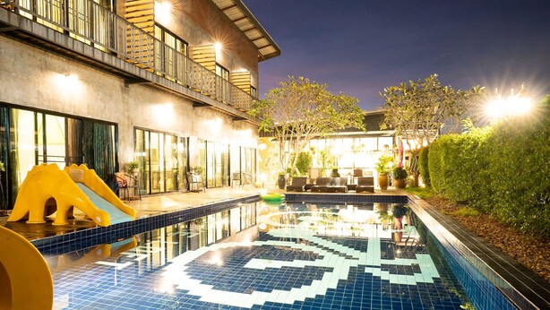 A swimming pool with a geometric tile pattern, a slide, and outdoor seating. - The Bike Loft Family Hostel (Hua Hin)