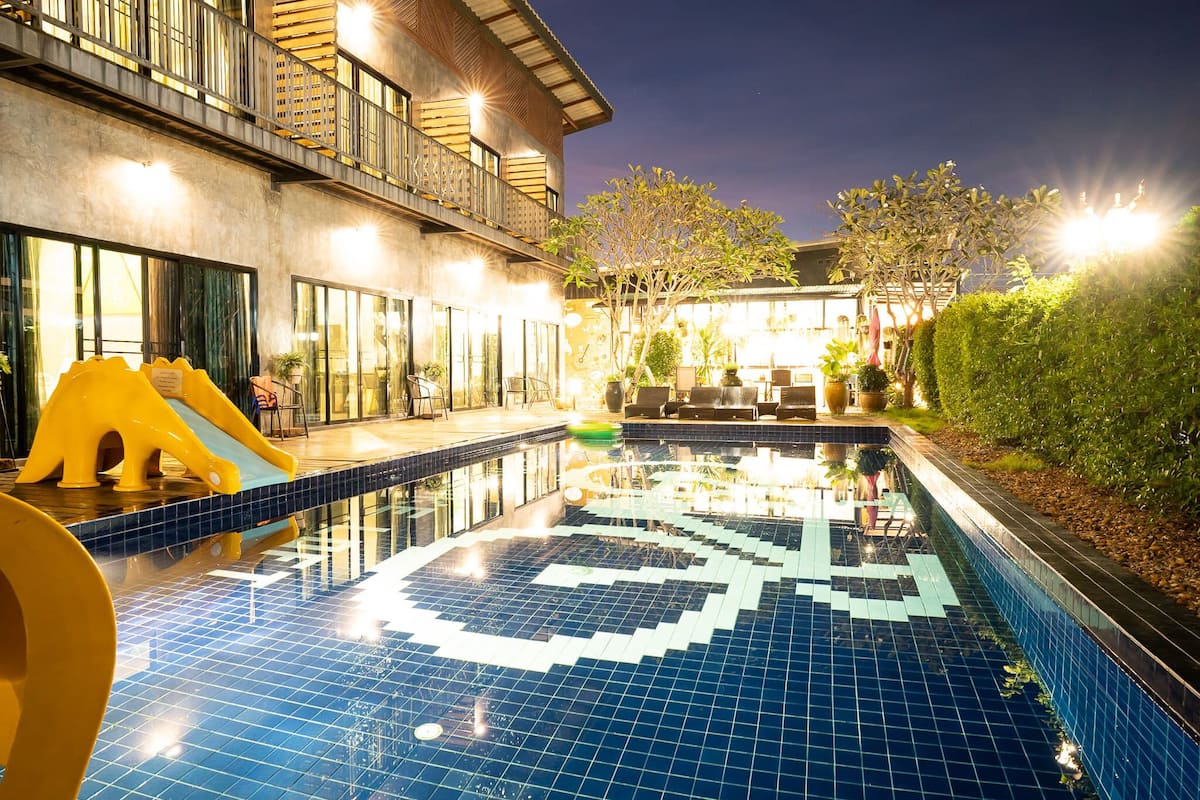 A swimming pool with a geometric tile pattern, a slide, and outdoor seating.