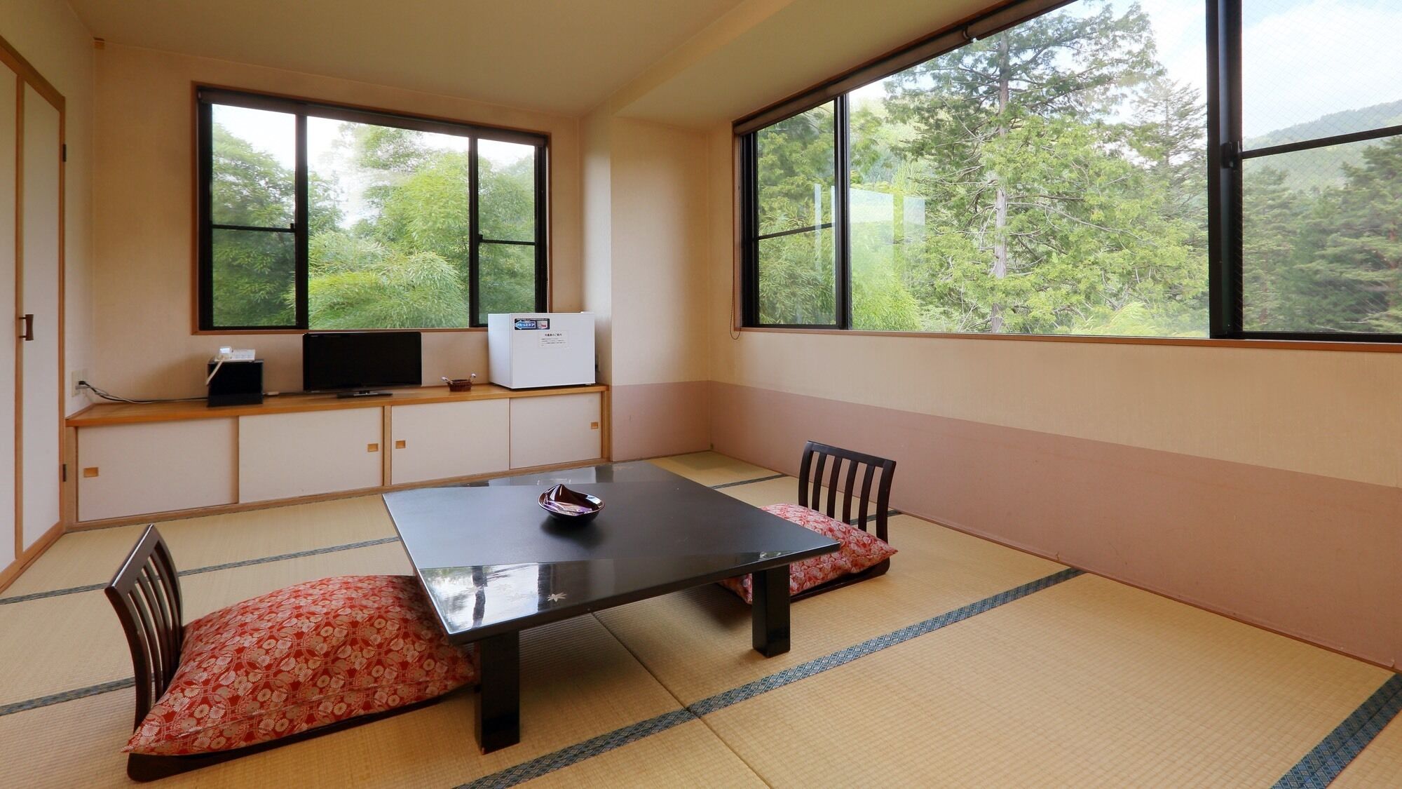 A tatami mat room with a low table, two chairs, a television, and a refrigerator.
