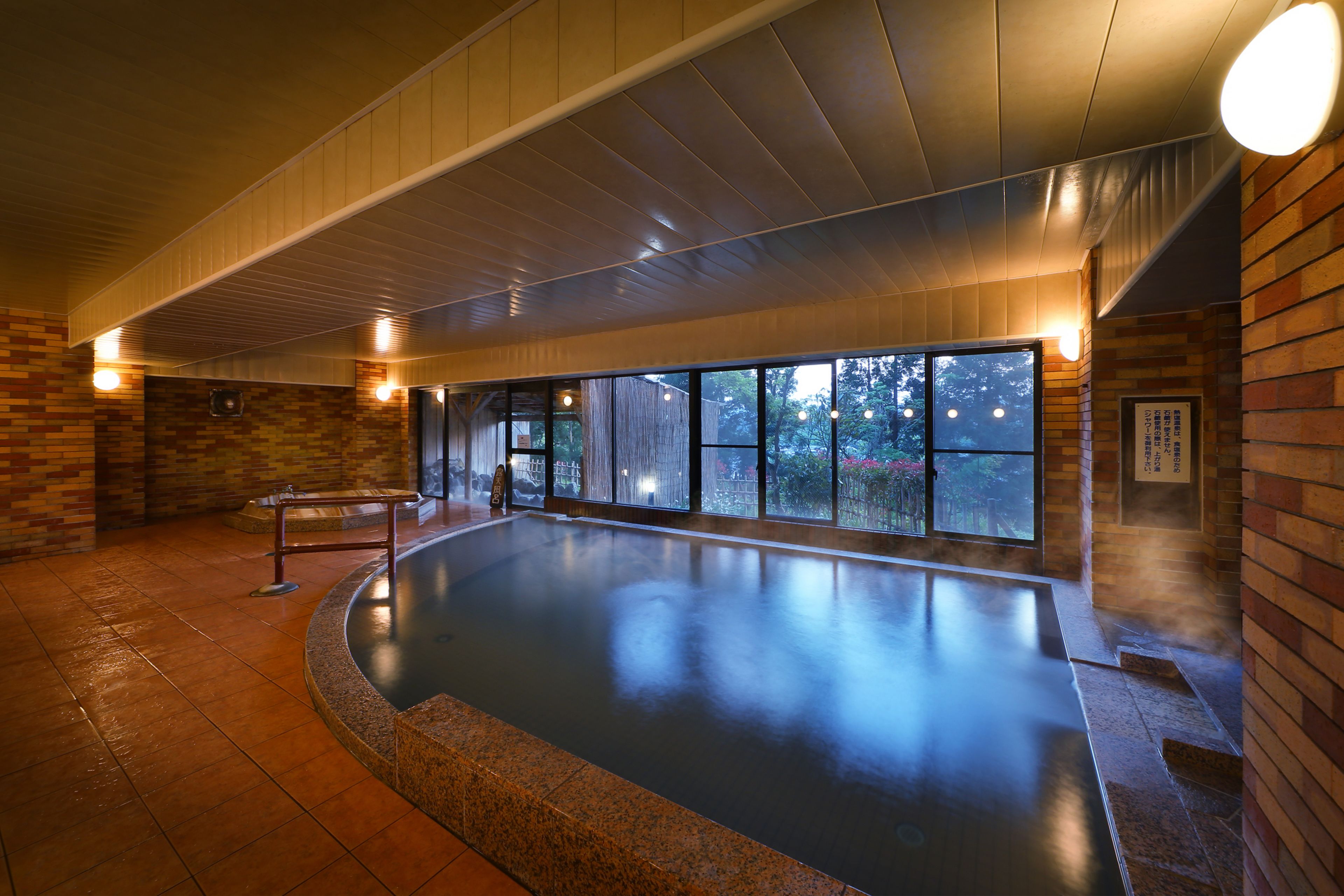 Una piscina interior con suelo de baldosas, paredes de madera y grandes ventanales.